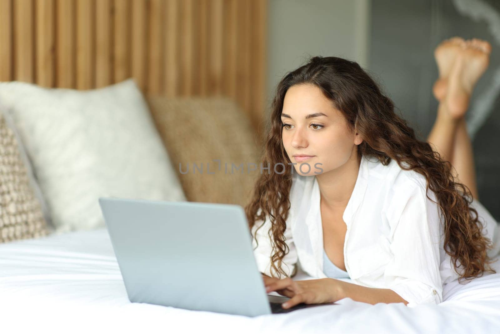Woman lying on a hotel bed checking laptop
