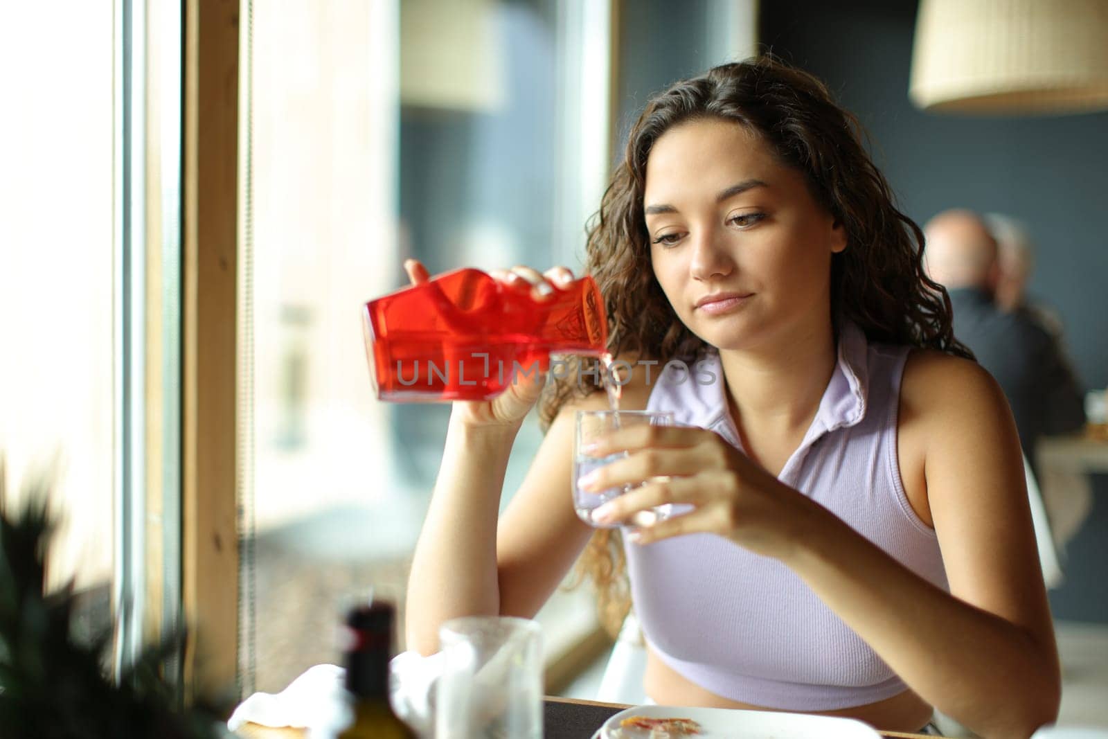 Woman filling glass of water from bottle sitting in a restaurant
