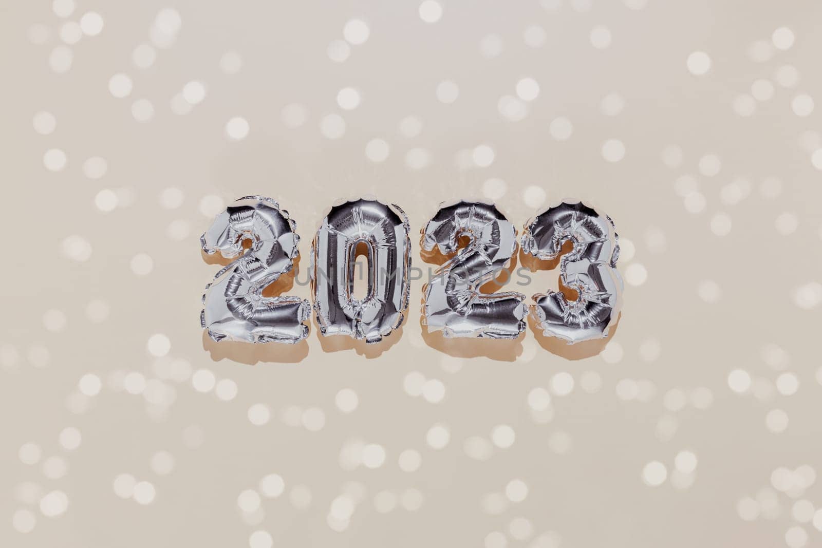 Christmas or New Year background. Beige color flat lay decorated with white paper glitter and silver shiny 2023 baloon numbers. Simple minimalistic greeting card.
