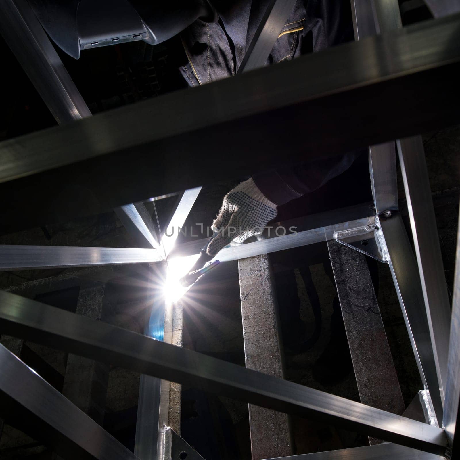 A skilled worker uses a welding torch to join metal beams in a dimly lit workshop, highlighting the intensity of the task.