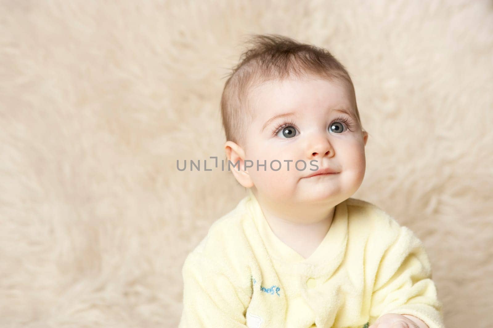 Sixth month old baby girl in yellow and blue clothes on wool rug texture background. Baby looking to upper right with critical focus on eyes.