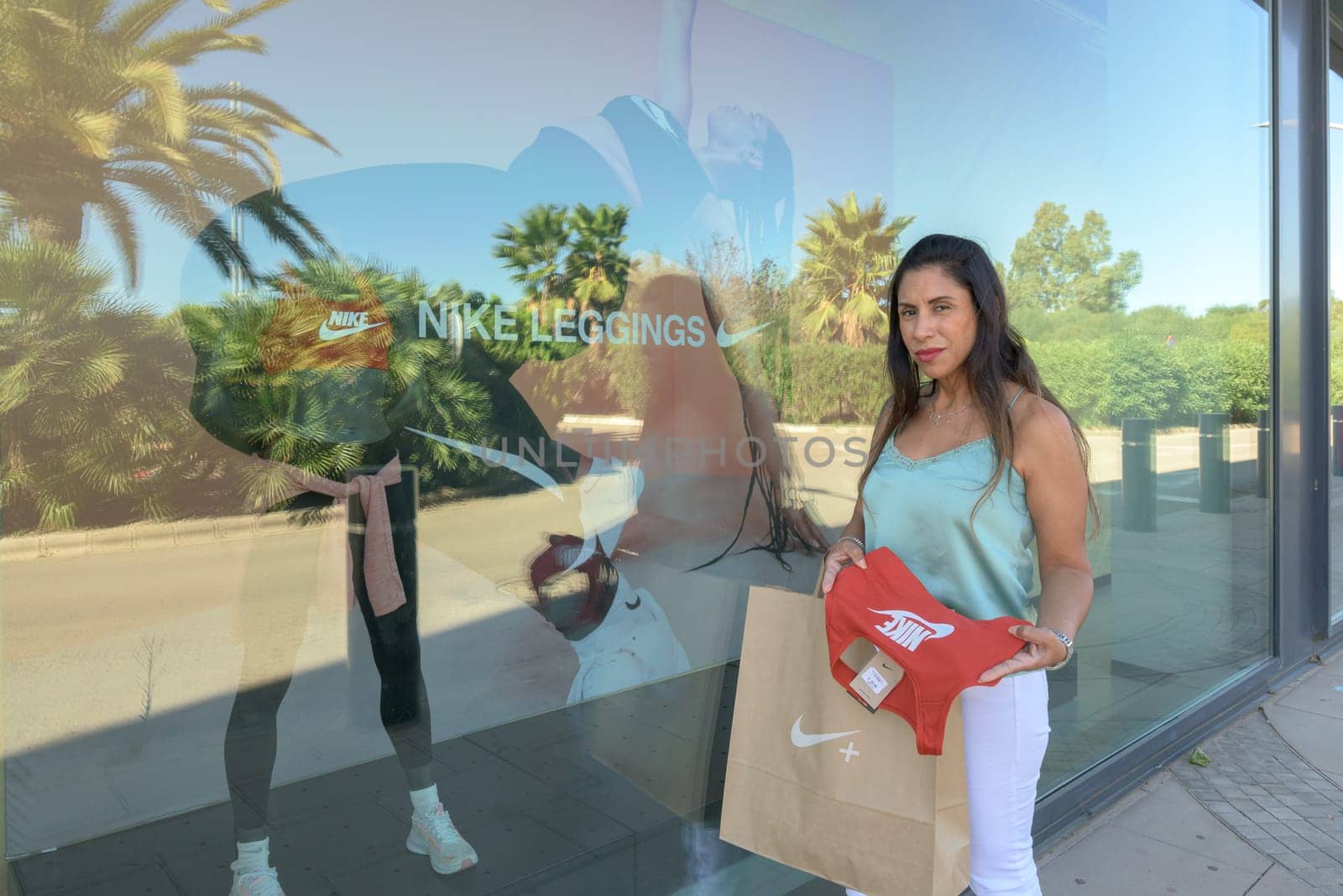 mallorca, balearic islands spain-november 05 2022: hispanic woman looking at the window of the nike sports store happy comparing the purchase made in the mall mallorca fashion outlet, on the outskirts of the city of palma
