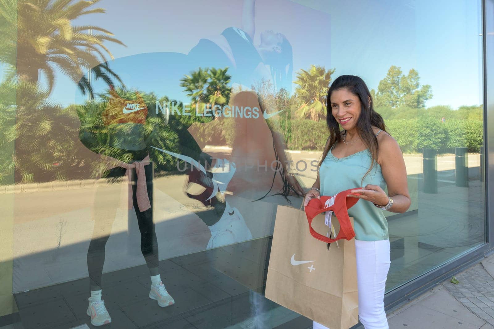 mallorca, balearic islands spain-november 05 2022: hispanic woman looking at the window of the nike sports store happy comparing the purchase made in the mall mallorca fashion outlet, on the outskirts of the city of palma