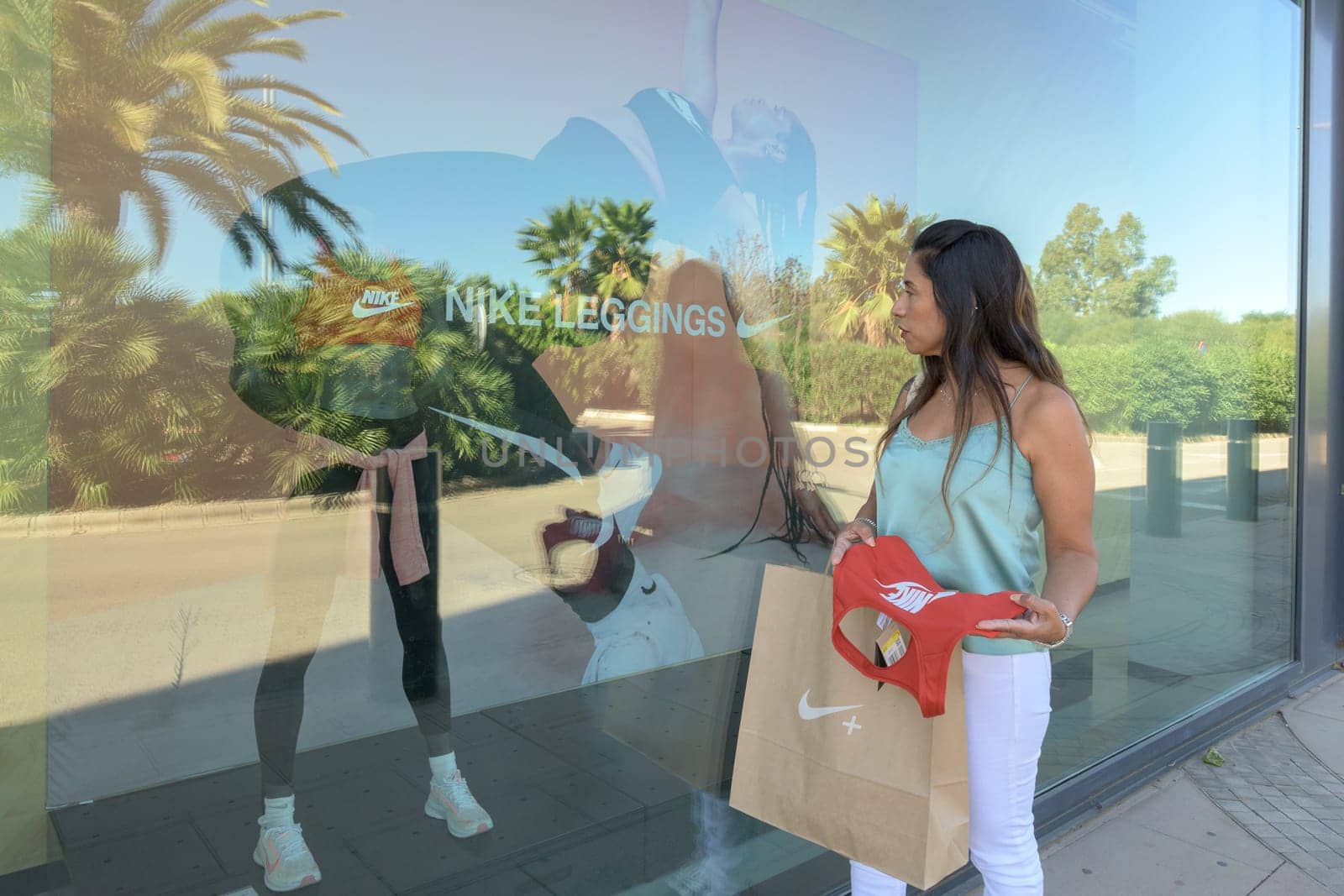 mallorca, balearic islands spain-november 05 2022: hispanic woman looking at the window of the nike sports store happy comparing the purchase made in the mall mallorca fashion outlet, on the outskirts of the city of palma