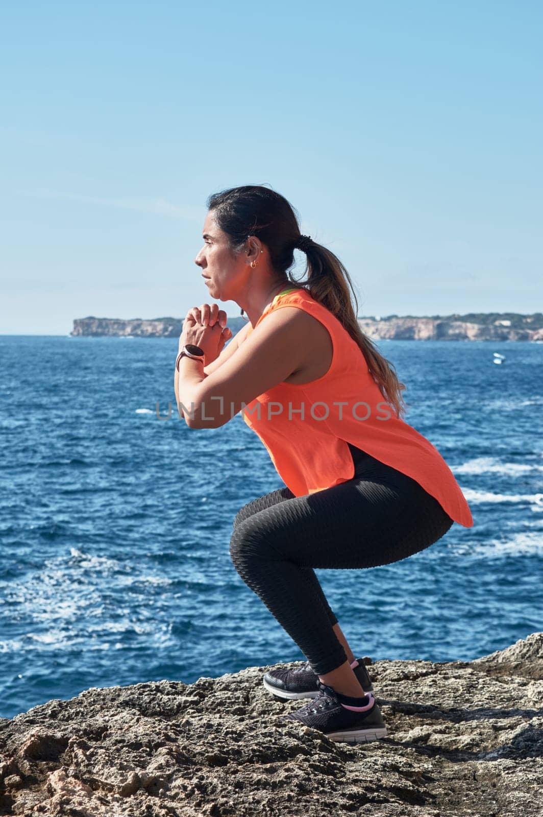 FITNESS WOMAN IN SPORTS SET TRAINING WITH ELASTIC BAND, WEIGHTS, GYM EXERCISES, IN FRONT OF THE WATER.