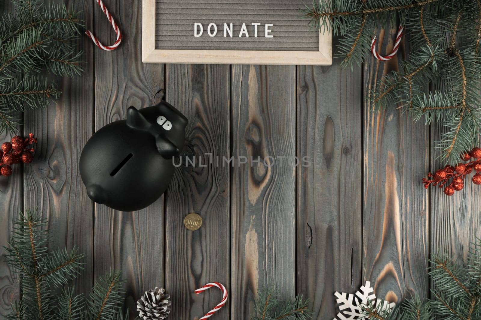Abstract holiday composition with black pig moneybox with golden coin in Christmas twigs and candies decoration. Charity, donation and altruism. Generosity in holidays. Flat lay, copy space, mockup