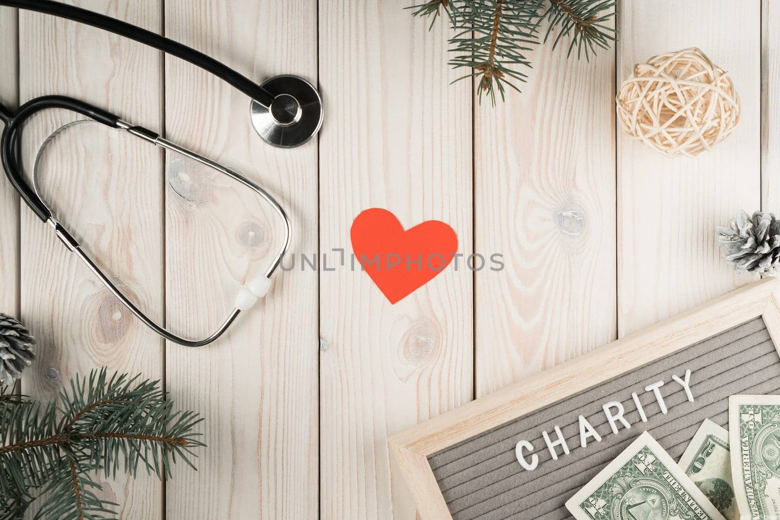 Abstract composition of nameplate charity with money, stethoscope, red heart and spruce twigs as decoration on wooden background. Healthcare and medicine, charity, donation. World health day. Top view