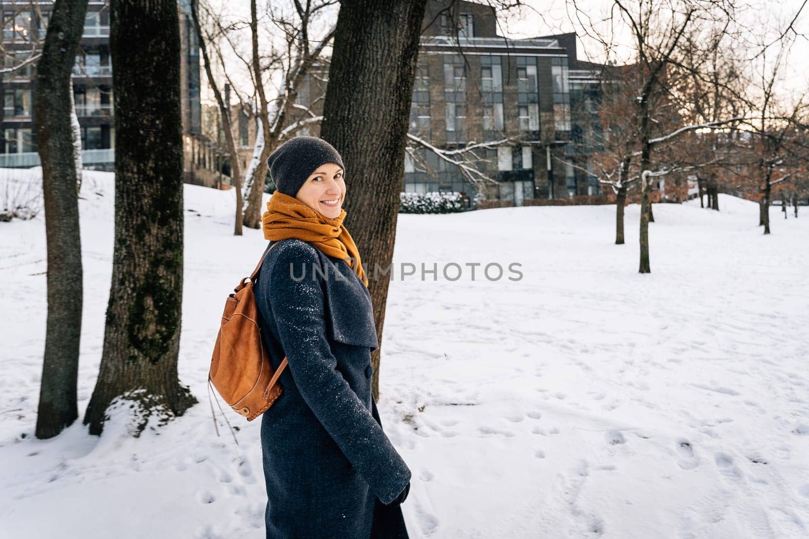 A woman in winter clothes with a leather red backpack looks around smiling.