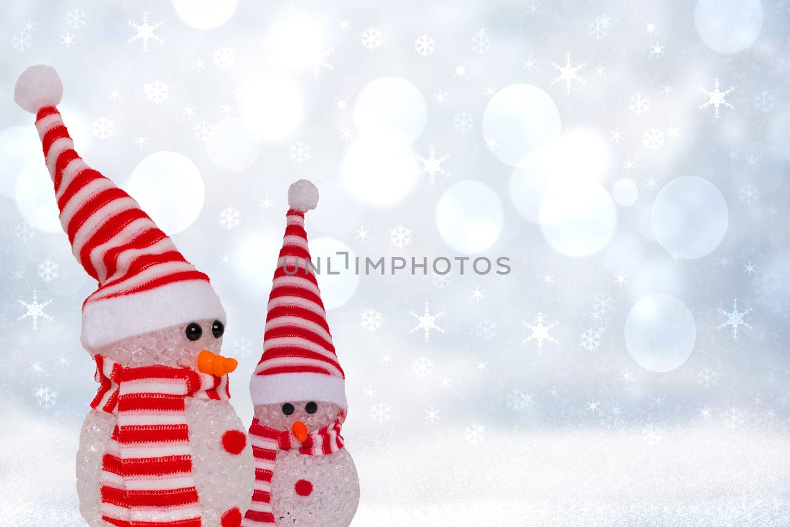 Christmas greeting card template. Xmas background texture with two cute winter snowman with red white striped hat and scarf in a abstract snowy winter landscape. Space.