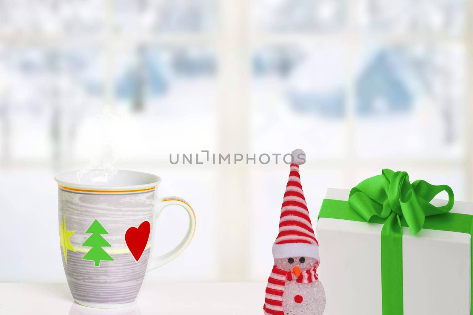 Merry Christmas and Happy New Year greeting card. A snowman, a gift package and a Christmas cup on the table in front of abstract winter landscape. Space for text.