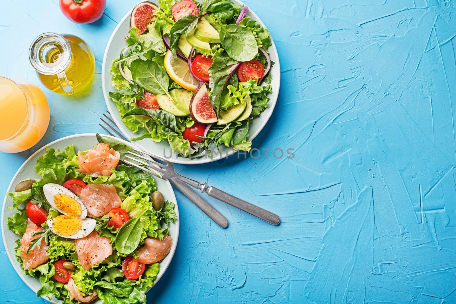 Fresh green lettuce salads with smoked salmon, cherry tomatoes, egg and avocado on blue table background