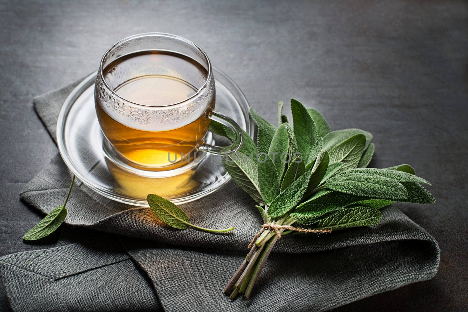 Sage tea in glass mug and sage leaves on grey table close up