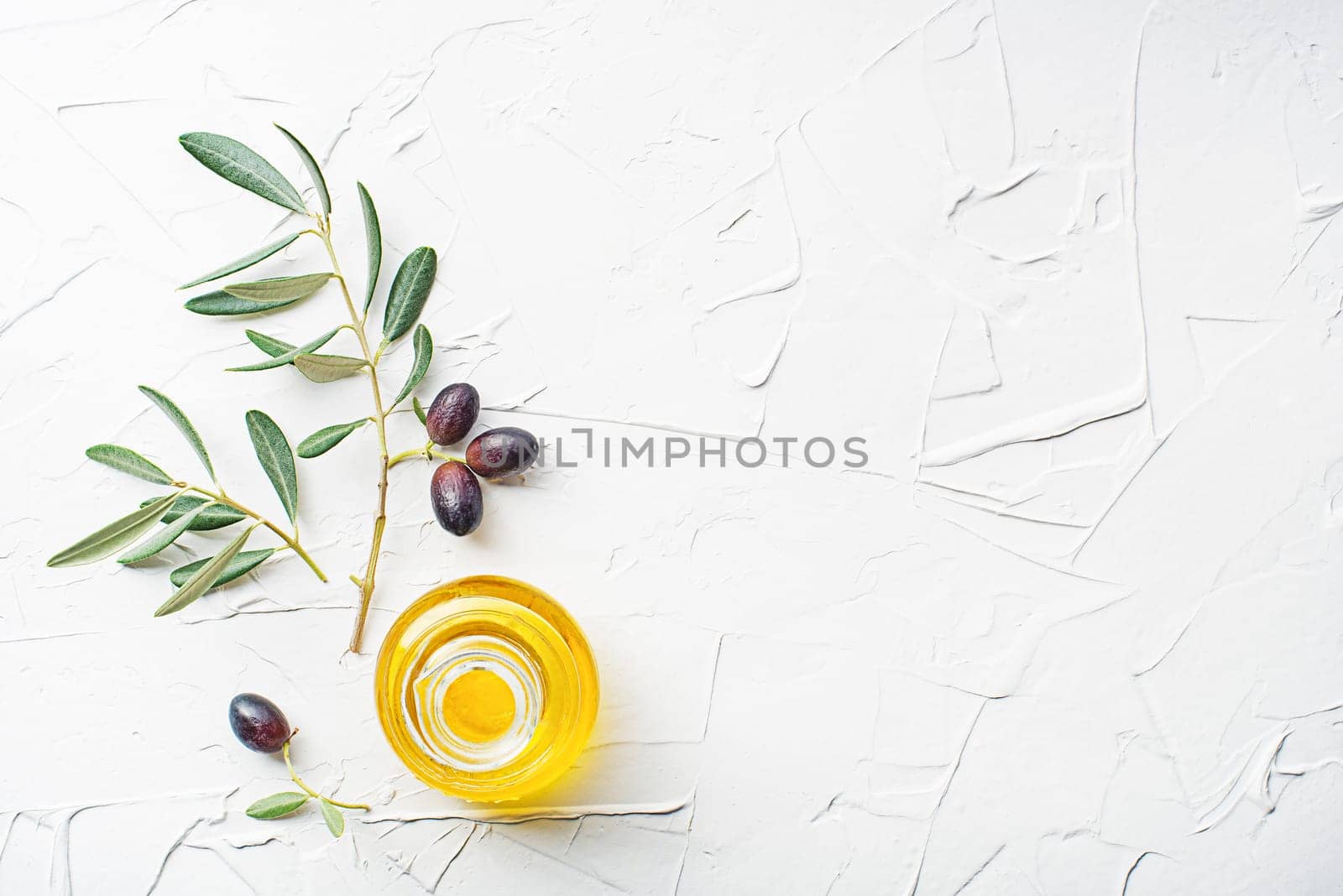Olive oil in bowl with fresh olives fruit and olive branch on white background close up