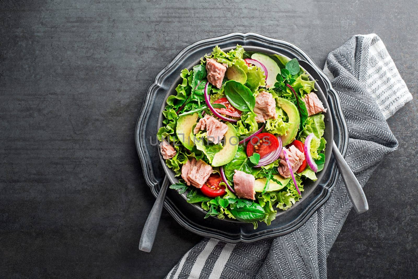Fresh green leafy salad with tuna avocado and tomato on grey table background. Concept for a tasty and healthy meal