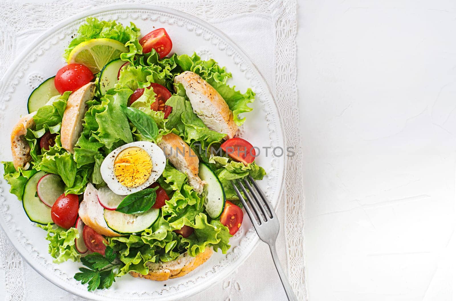 Fresh green salad with chicken breast vegetable and boiled egg on white background close up