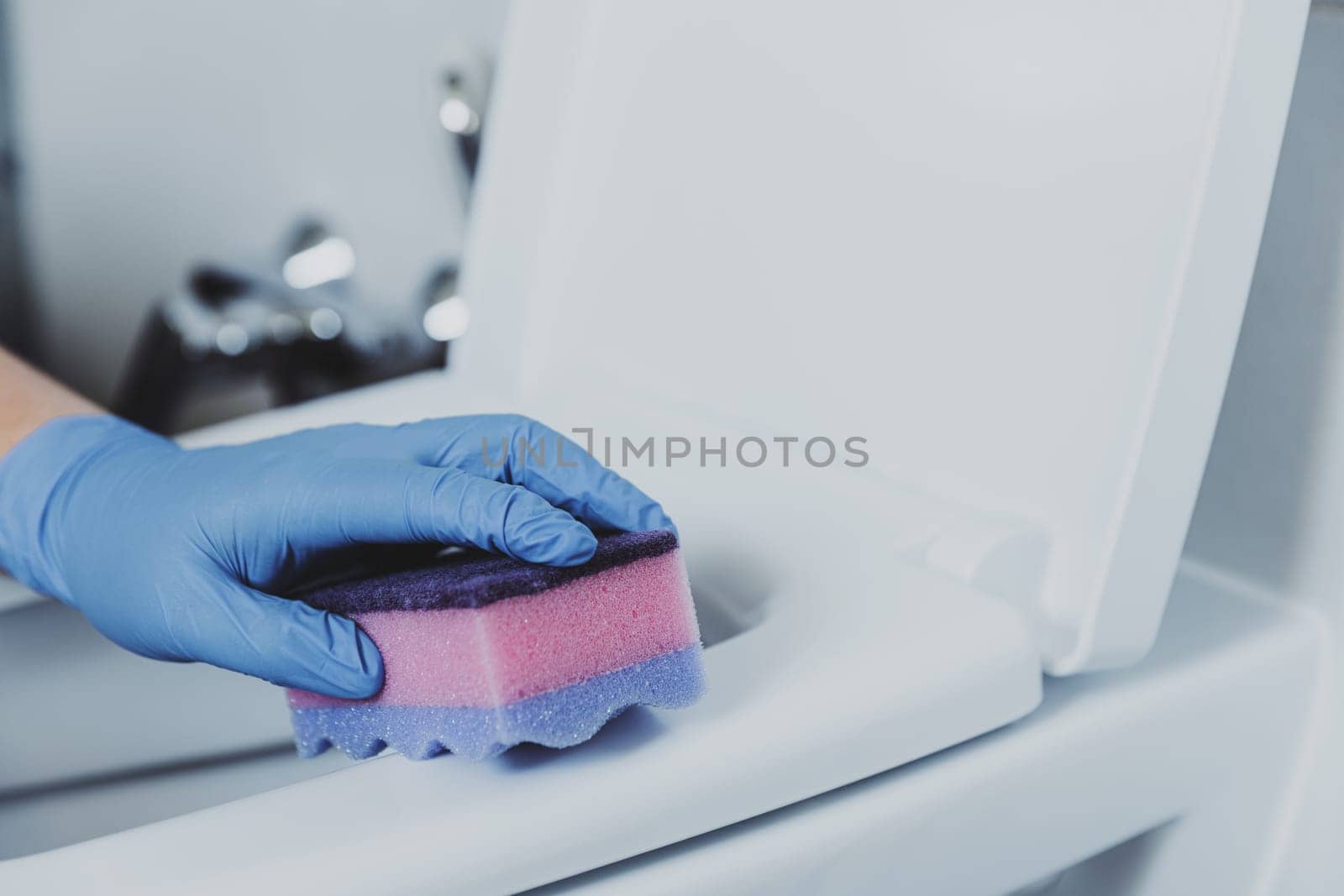 Woman hand closeup gloved in rubber protective gloves. Housewife cleaning toilet bowl, seat with detergent, pink cloth in bathroom or public restroom. Disinfection, hygiene, cleaning service concept
