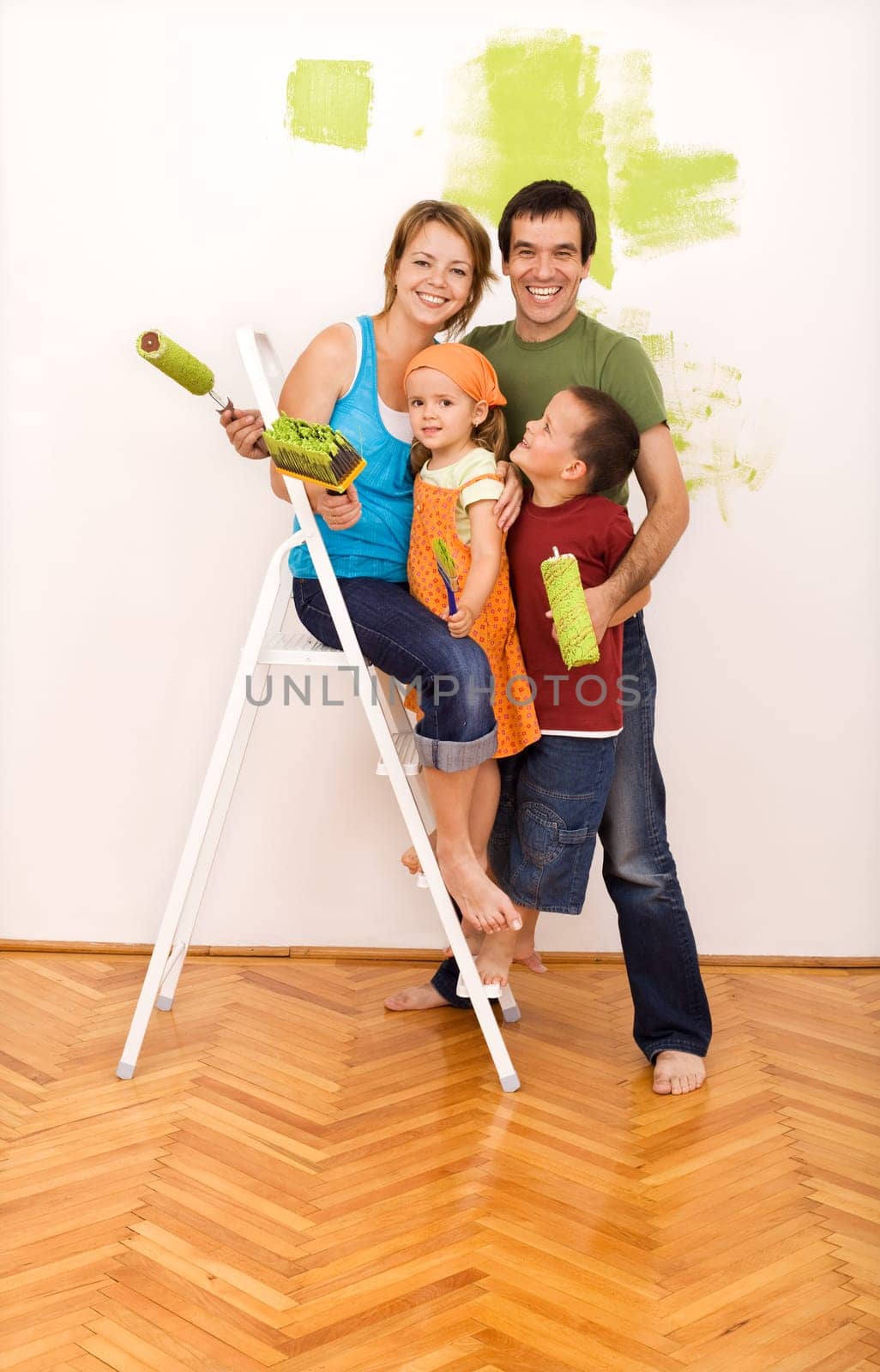 Happy family with two kids on a ladder painting their new home together