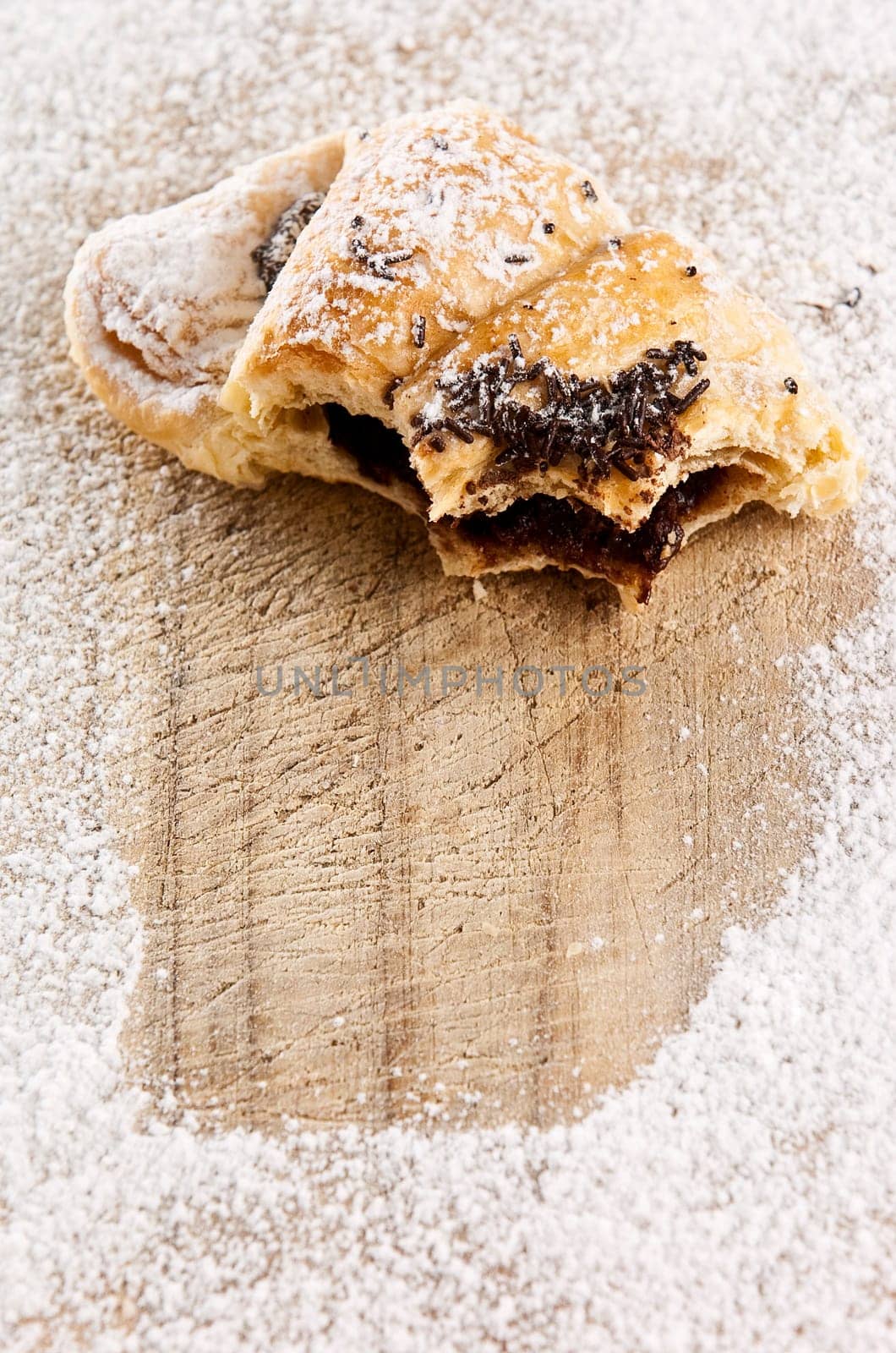 A half eaten chocolate croissant sprinkled with sugar