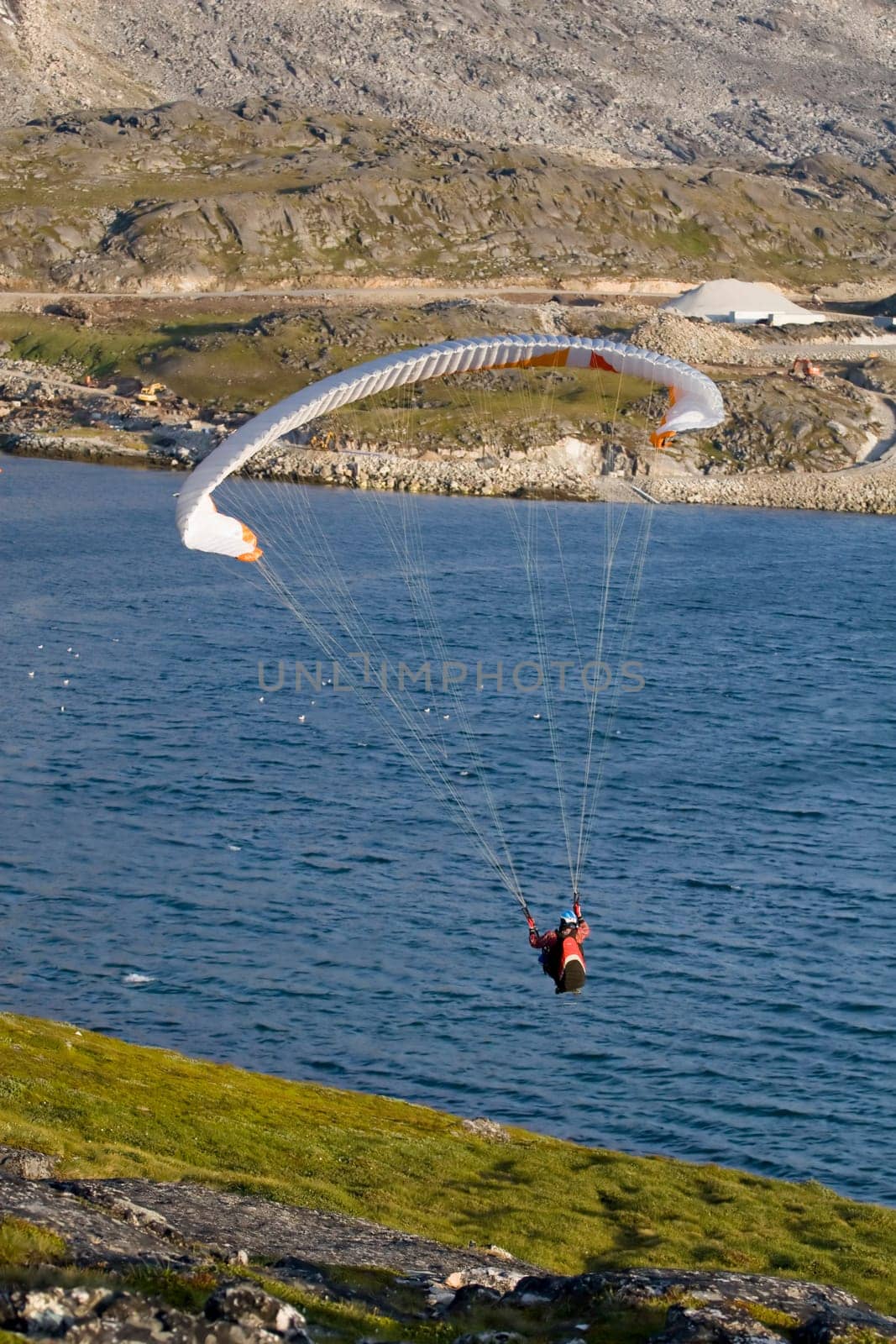 Paraglider hanging over the ocean. There is a mountain face in the background.