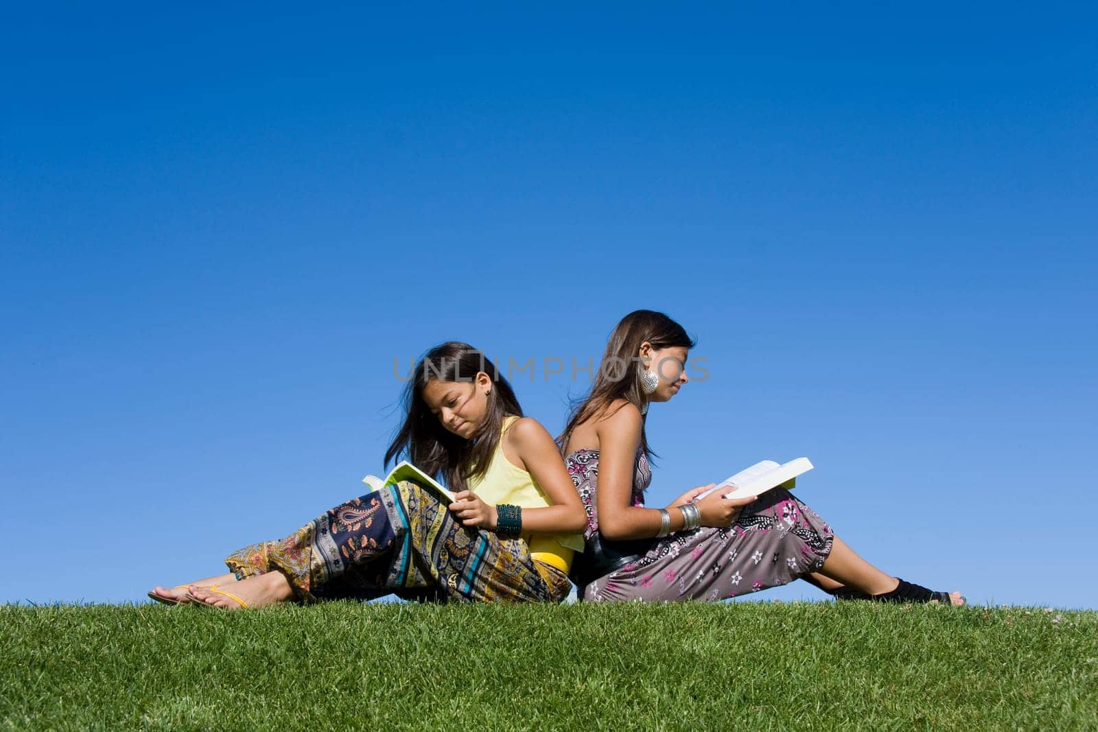 Two young girls reading isolated on blue sky