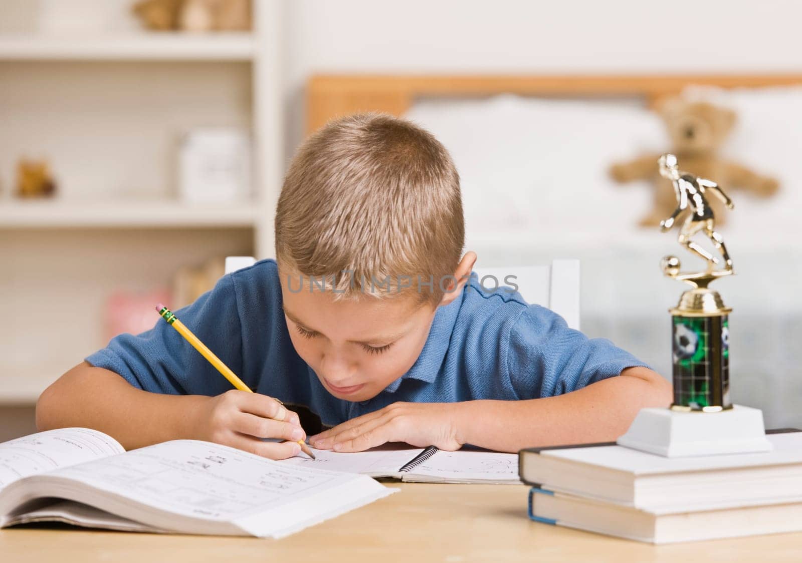 A young boy is working on his homework at the table.  He is looking away from the camera.  Horizontally framed shot.