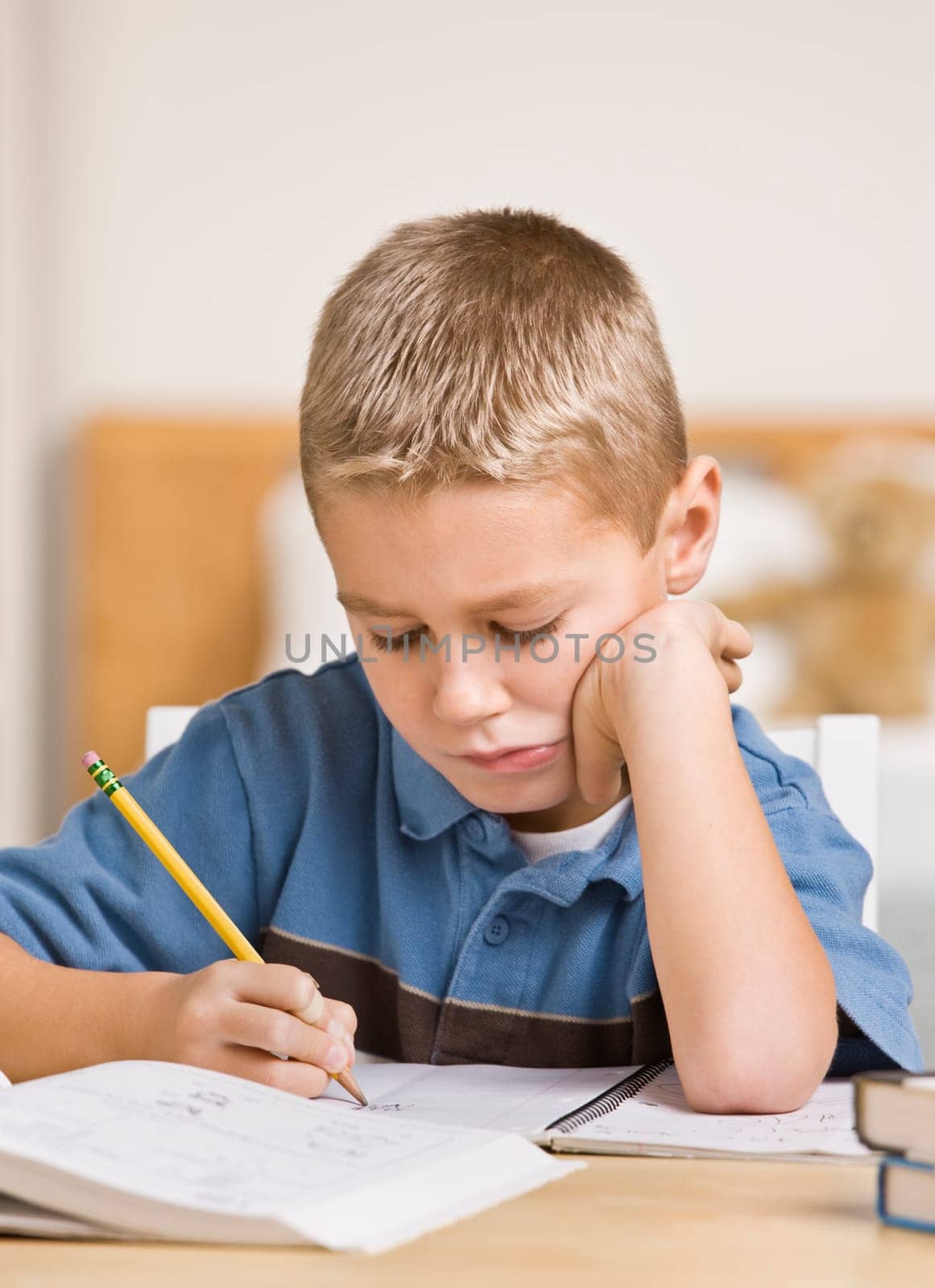 A young boy is working on his homework at the table.  He is looking down at what he is doing.  Vertically framed shot.