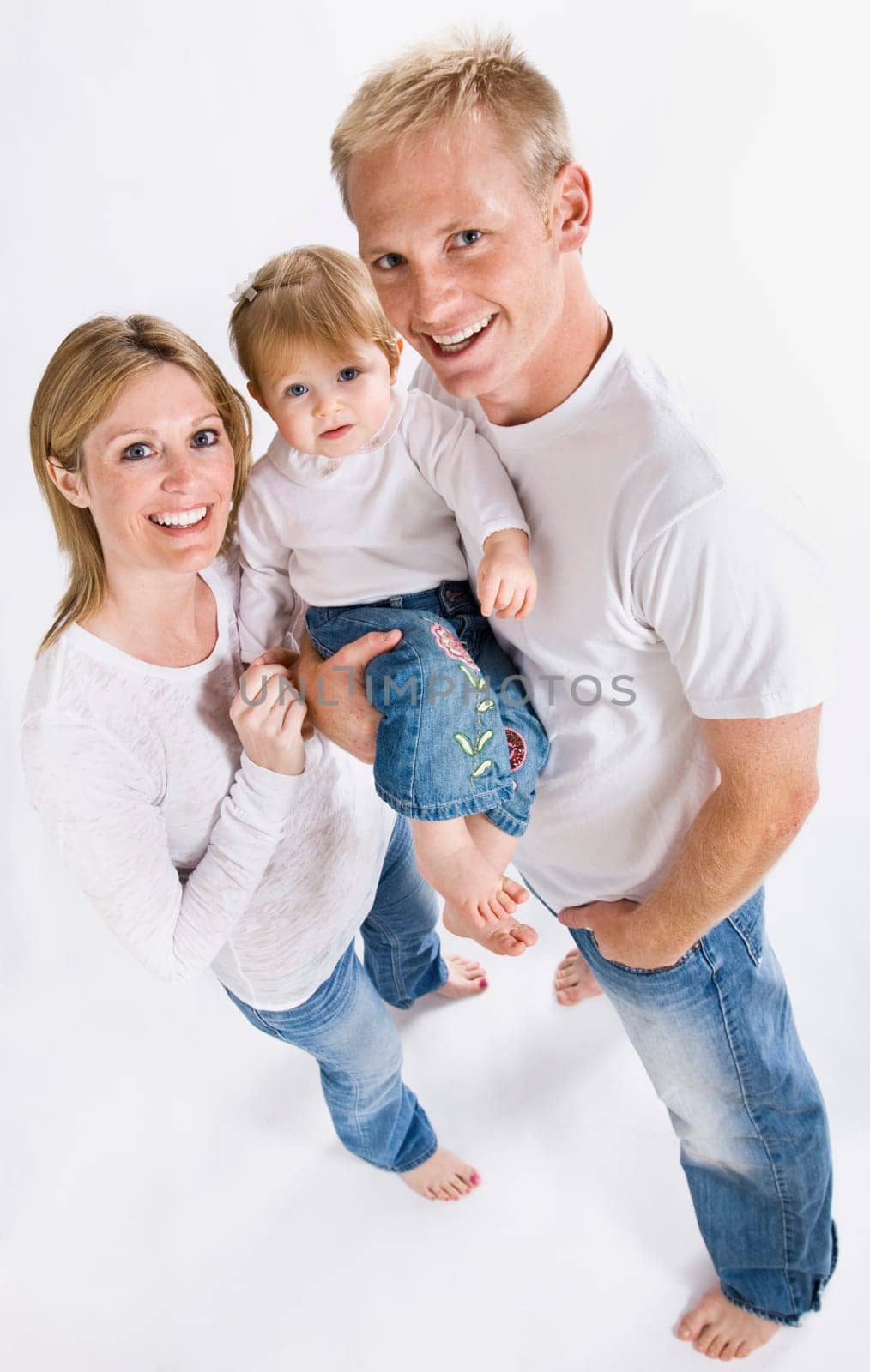 A young family is wearing white T-shirts and smiling up at the camera.  Vertically framed shot.