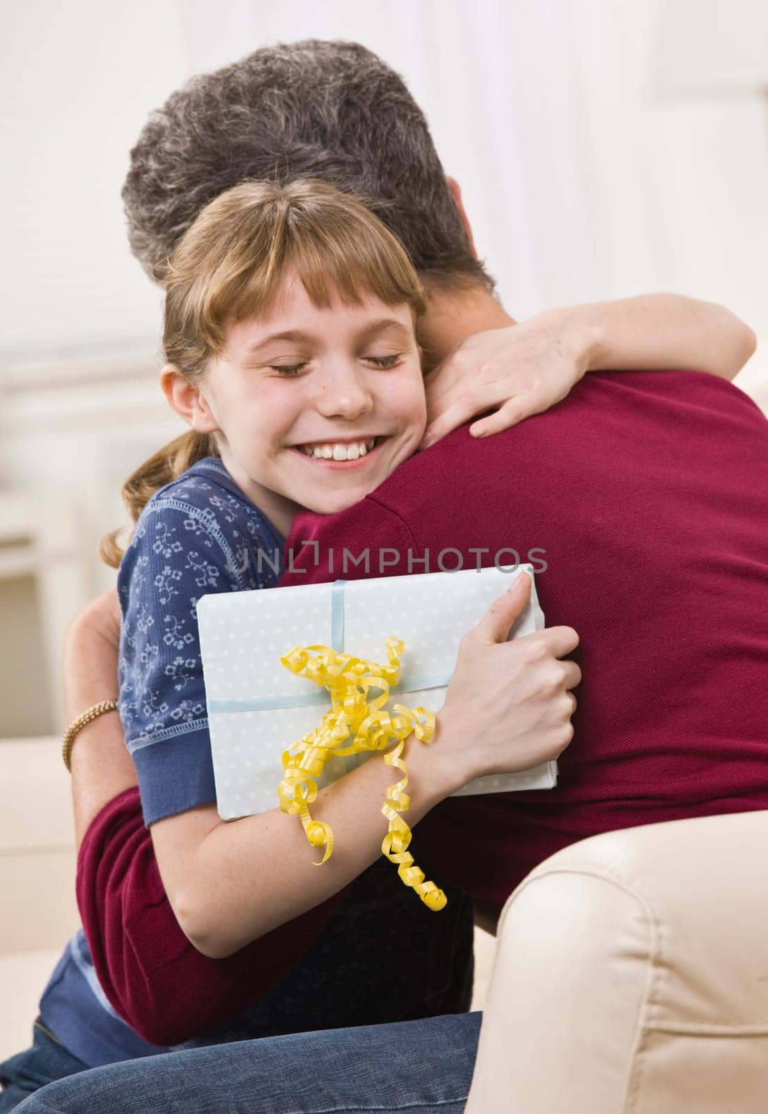 A young girl has received a gift from and is hugging her grandmother.  Vertically framed shot.