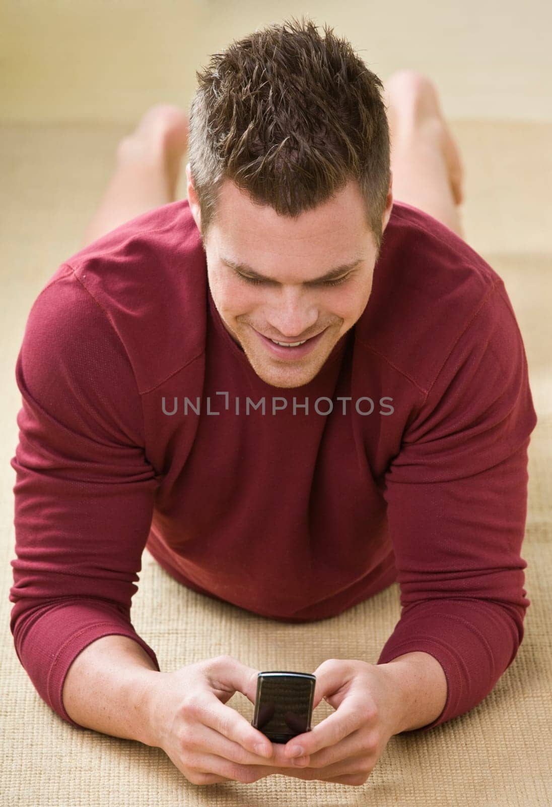 A man is holding a cell phone and is texting.  He is smiling and looking away from the camera.  Vertically framed shot.