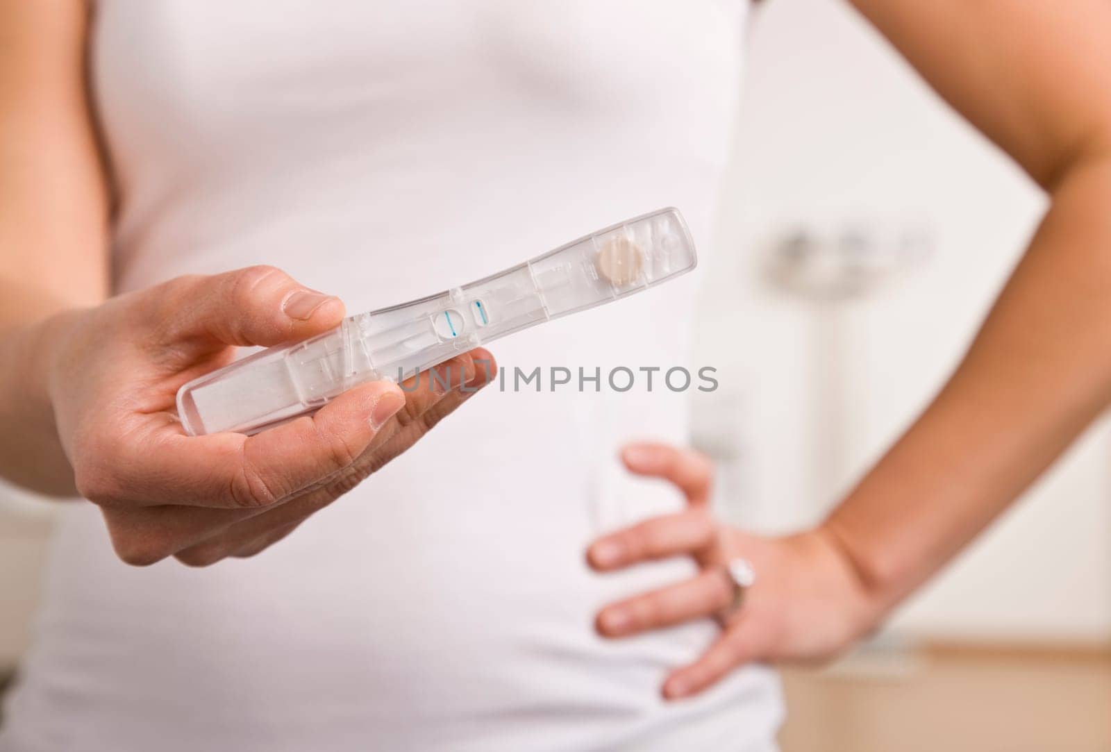 A woman is standing in her bathroom holding a pregnancy test in front of her.  Vertically framed shot.