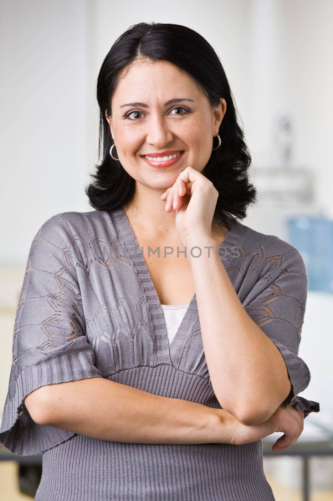 A young businesswoman is standing in an office and smiling at the camera.  Vertically framed shot.