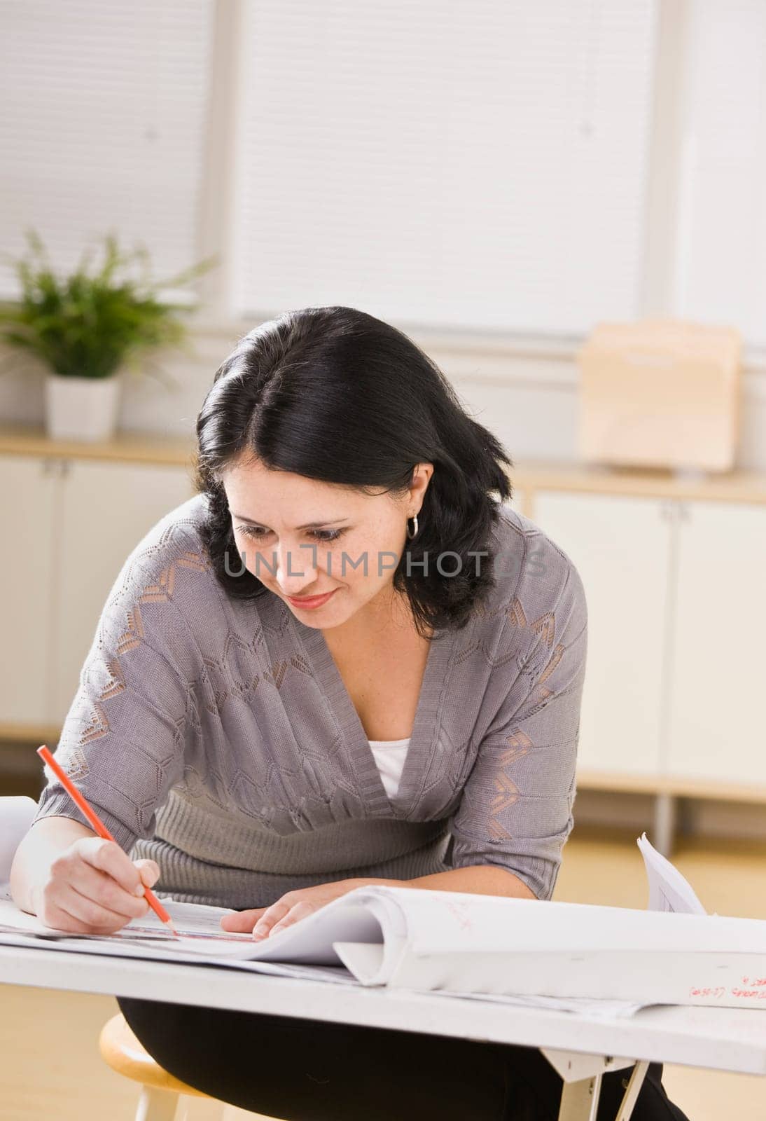 A young businesswoman is working on blueprints in an office.  She is looking away from the camera.  Vertically framed shot.
