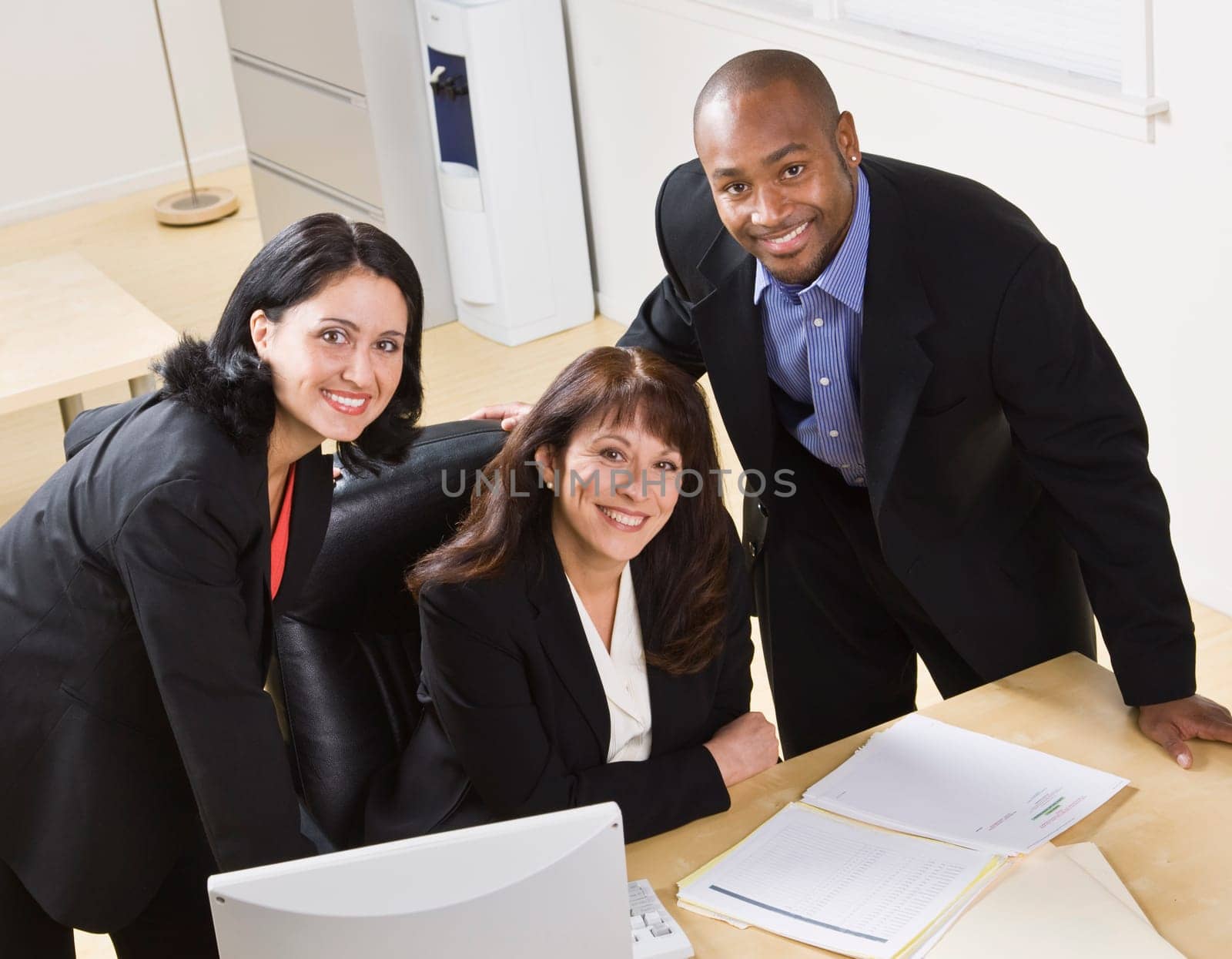 A group of business people are working together in an office.  They are smiling at the camera.  Horizontally framed shot.