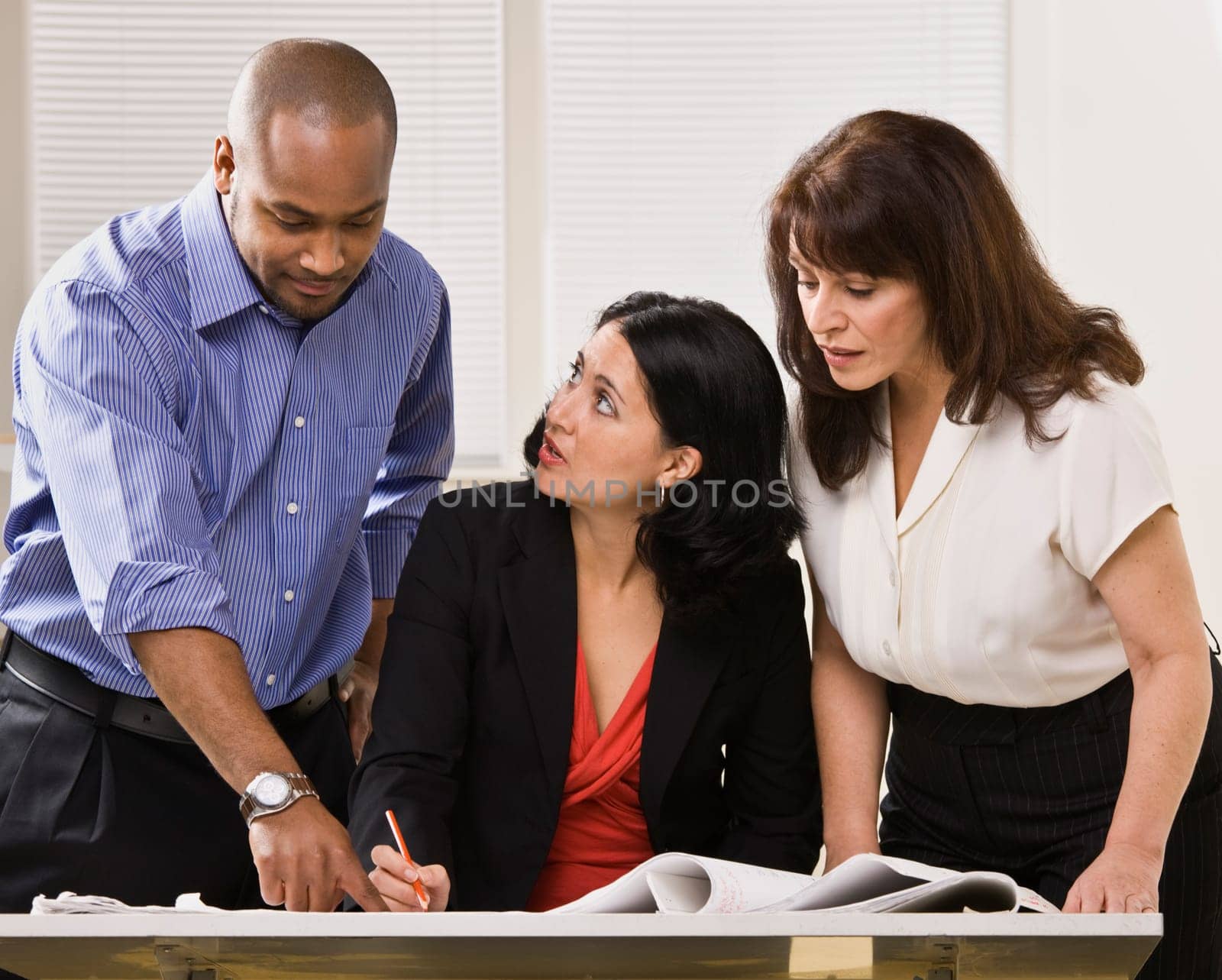 A group of business people are in an office and are looking at some paperwork.  They are talking and looking away from the camera.  Horizontally framed shot.