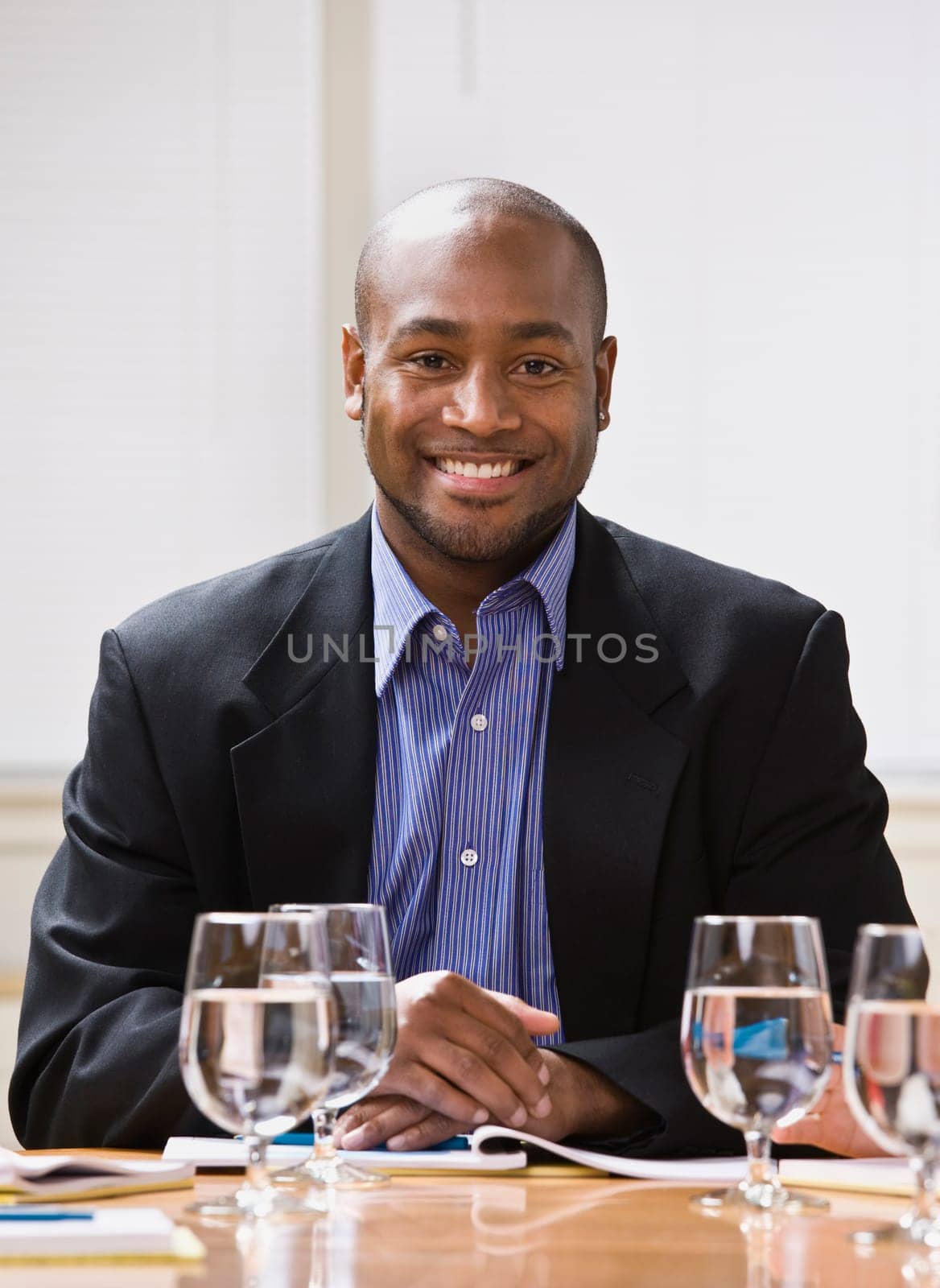 African American male sitting at desk with water, smiling at the camera. Vertical