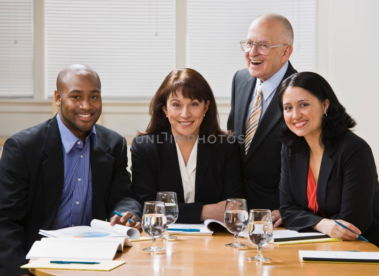 Four business workers, two men and two women, sitting at desk smiling at camera. Horizontal