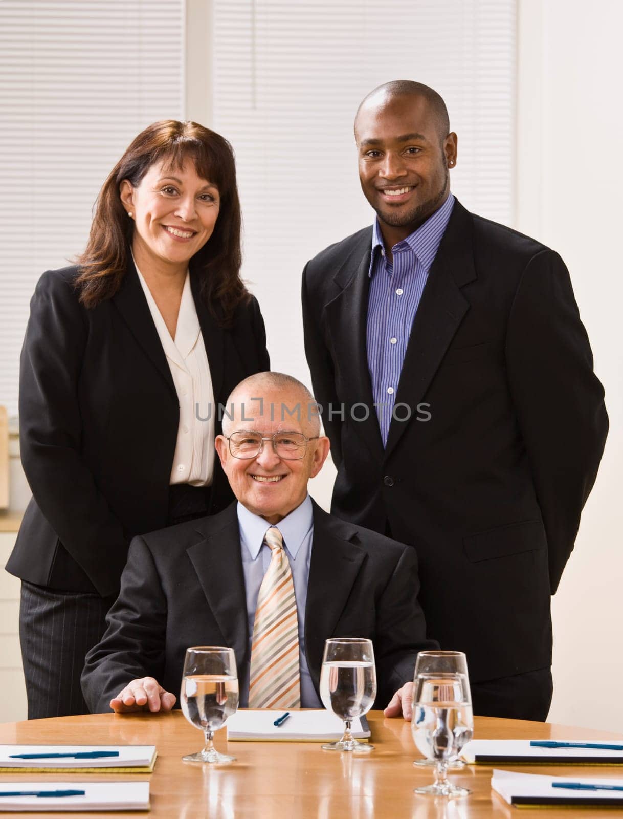 A group of business people are in an office and are smiling at the camera.  Vertically framed shot.