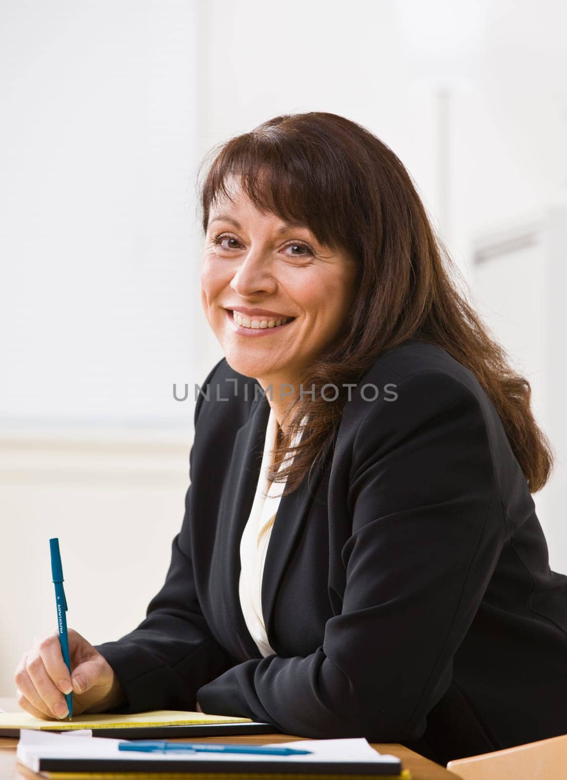 A businesswoman is seated at a desk and is smiling at the camera.  Vertically framed shot.