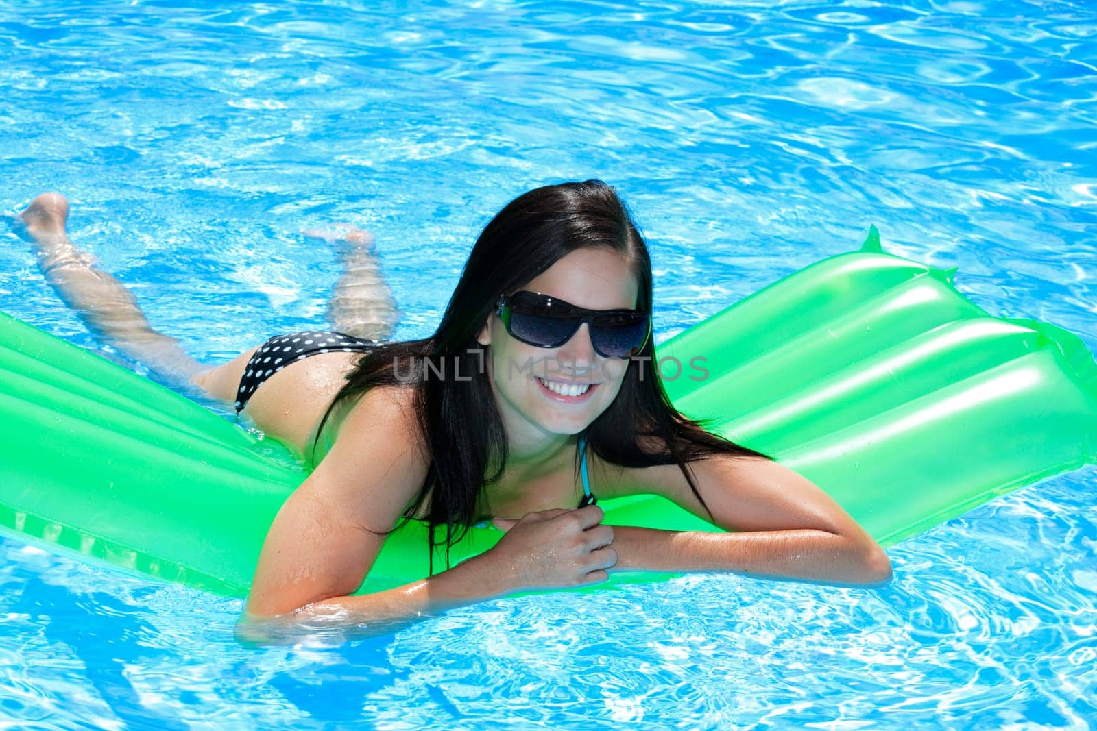 Attractive slim and tanned young lady lying on inflatable sunbed on sunny swimming pool on vacation or holiday