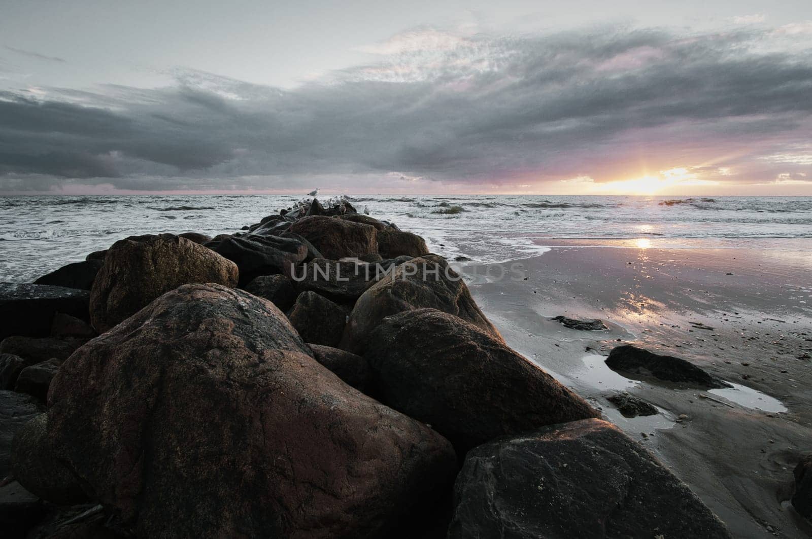 Sunset on the beach in Denmark. Stone groyne in the foreground. Walk on the coast in the sand. Landscape photo by the sea