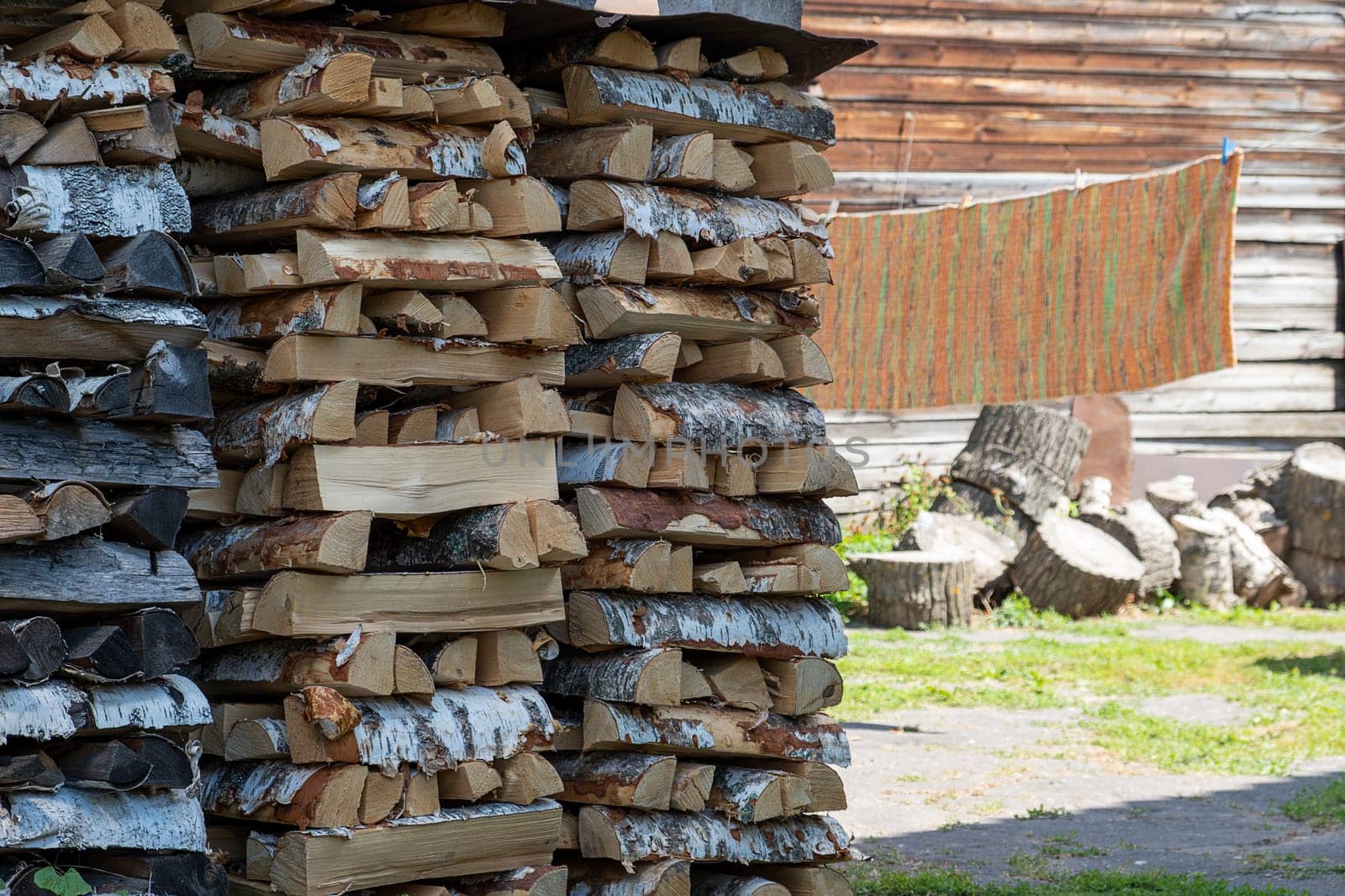 A woodpile of firewood in a rural area, against a village yard on a sunny summer day. Selective focus.