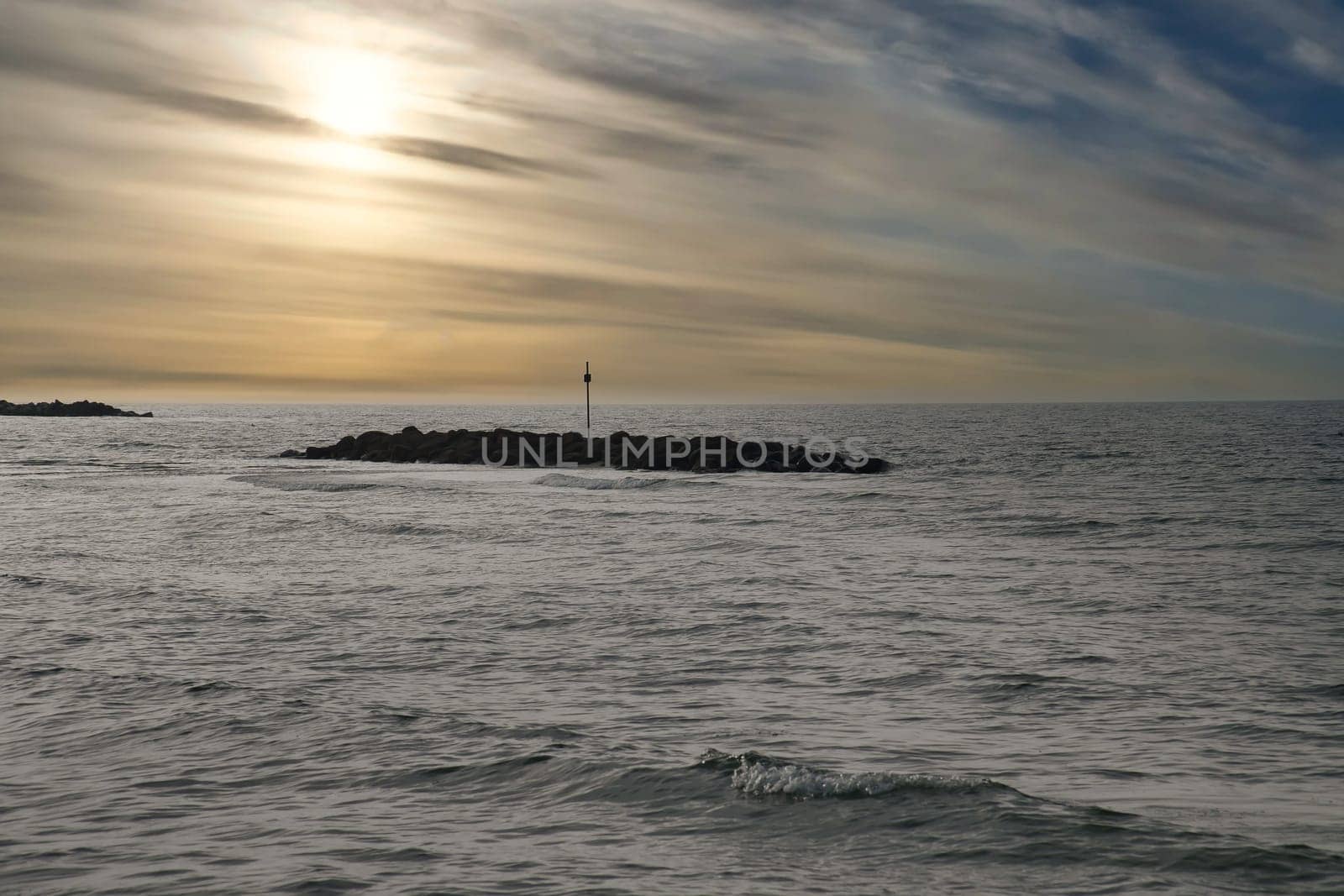 Stone groynes, breakwaters in the water off the coast in Denmark. In the evening with clouds in the sky. Landscape photo by the sea