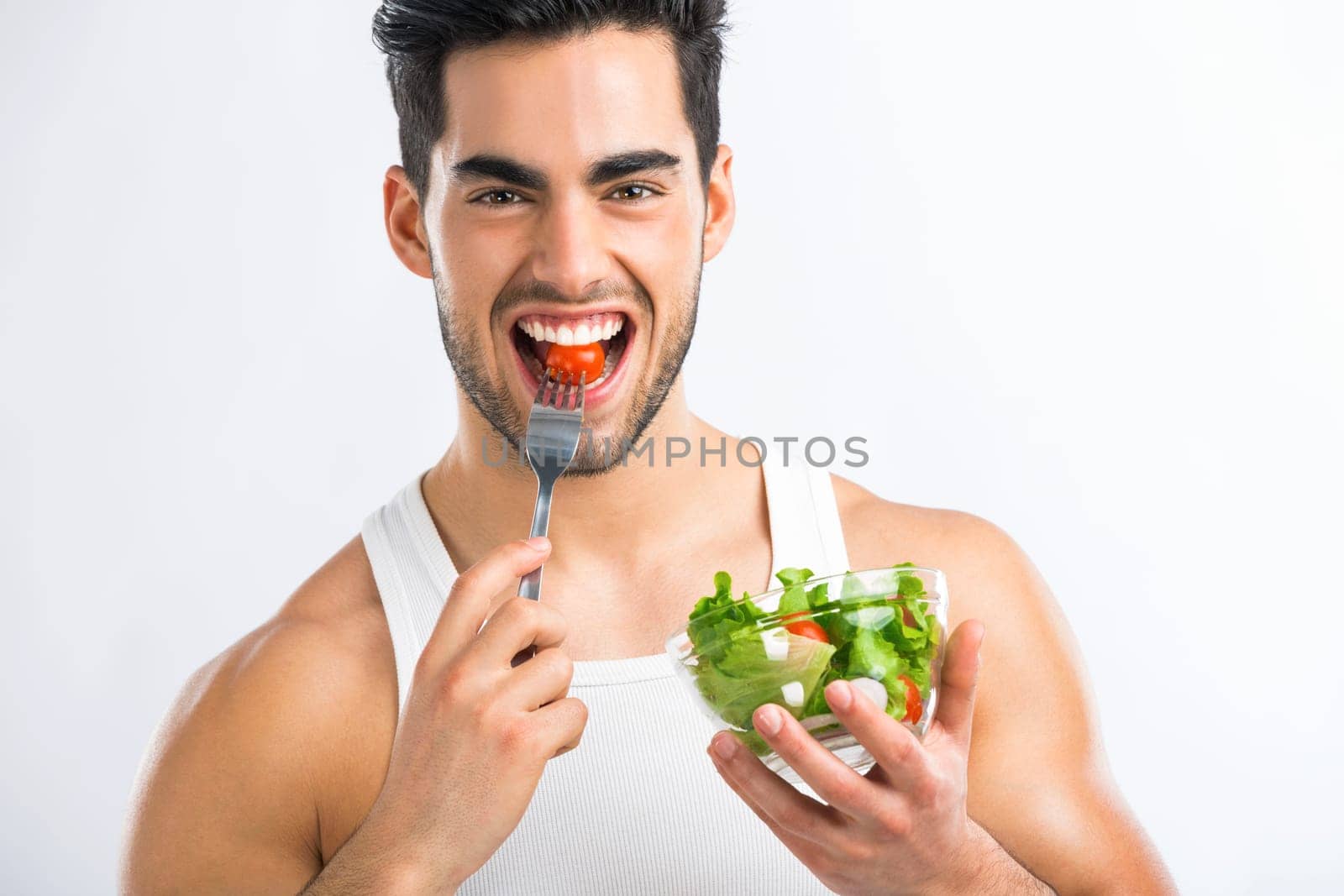 Handsome young man eating a healthy salad, isolated over a gray background