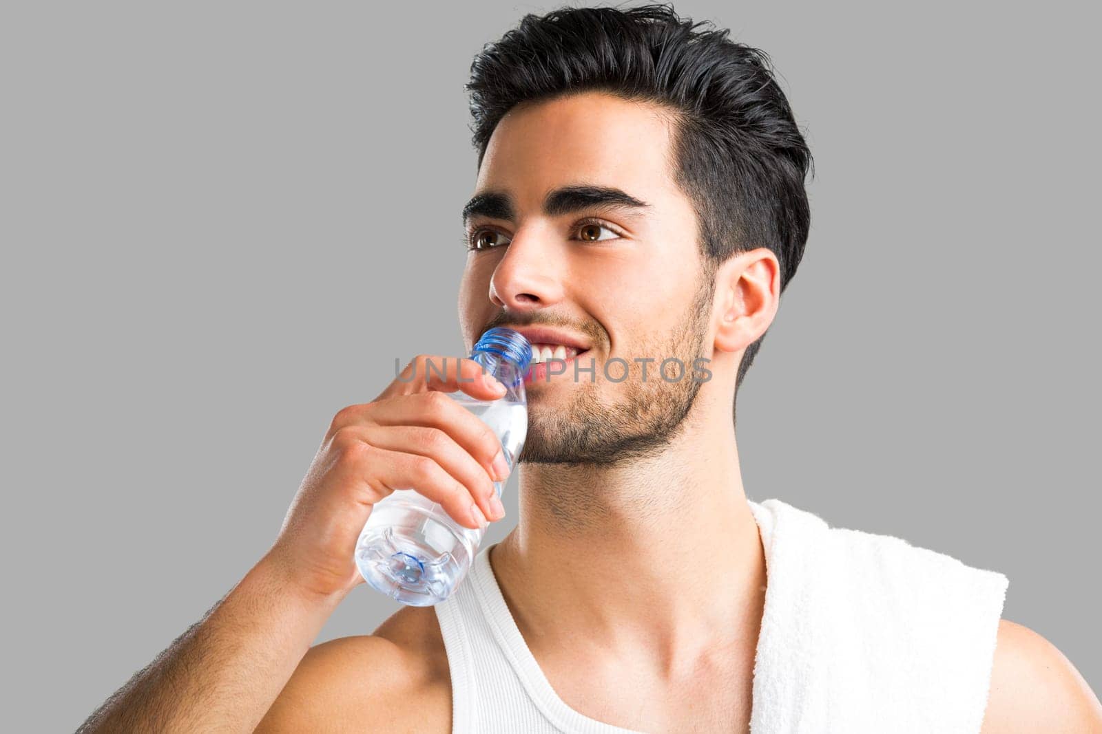 Portrait of a athletic young man drinking water, isolated over a gray background