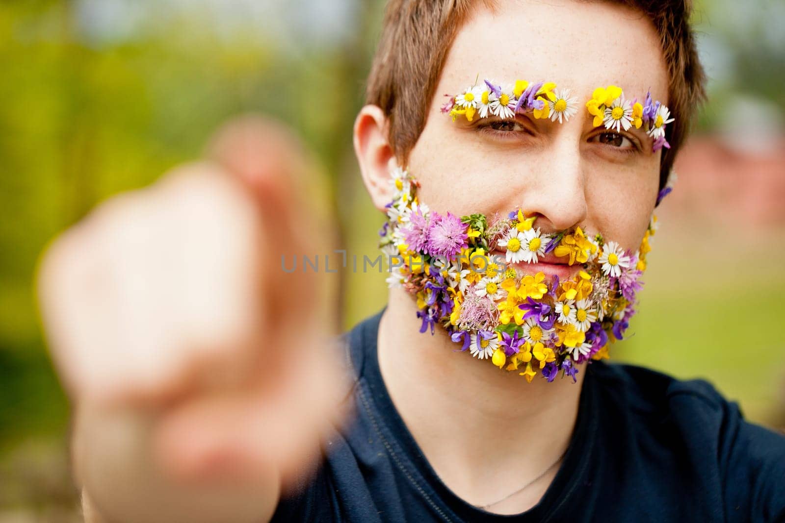 young hipster man with flowers instead of his face hair pointing out his finger asking us to act