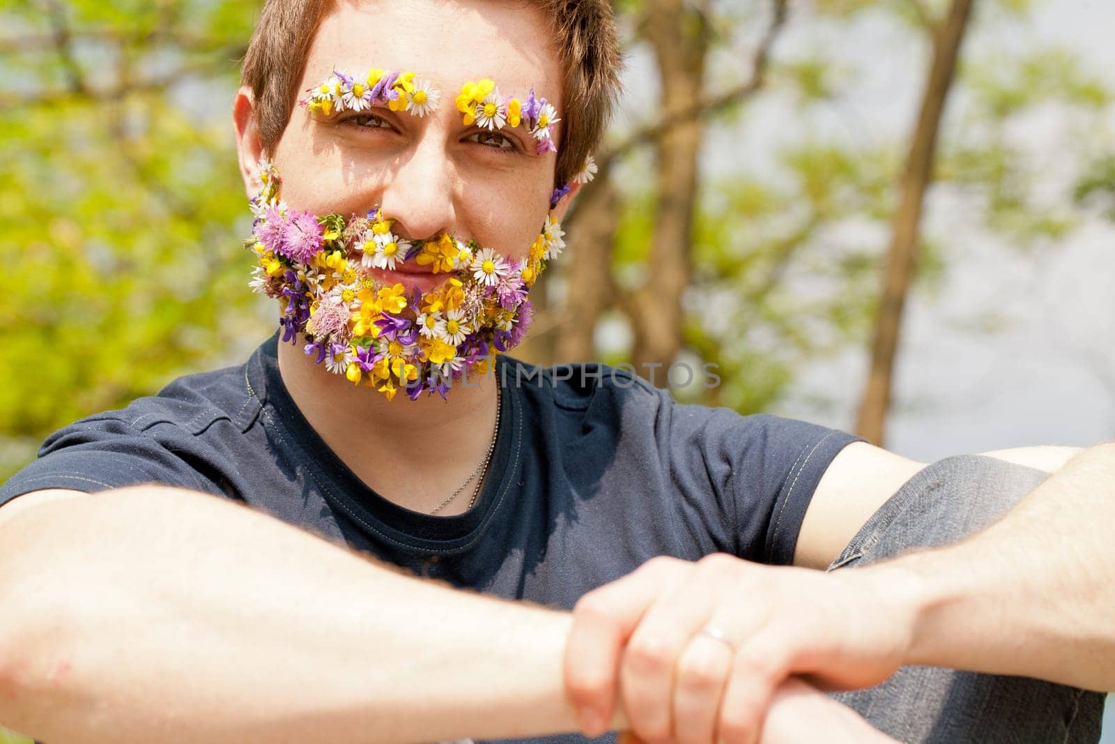 young self-confident man looking at camera with his eyebrow and beard disguised with flowers