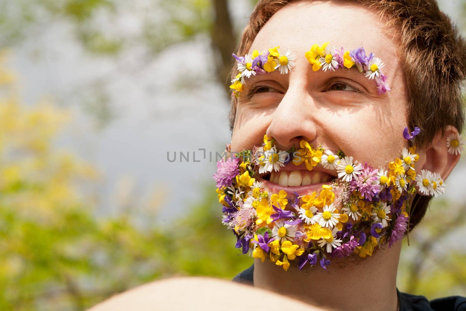 young man with his face covered with flowers and an hipster appereance smiling outdoors