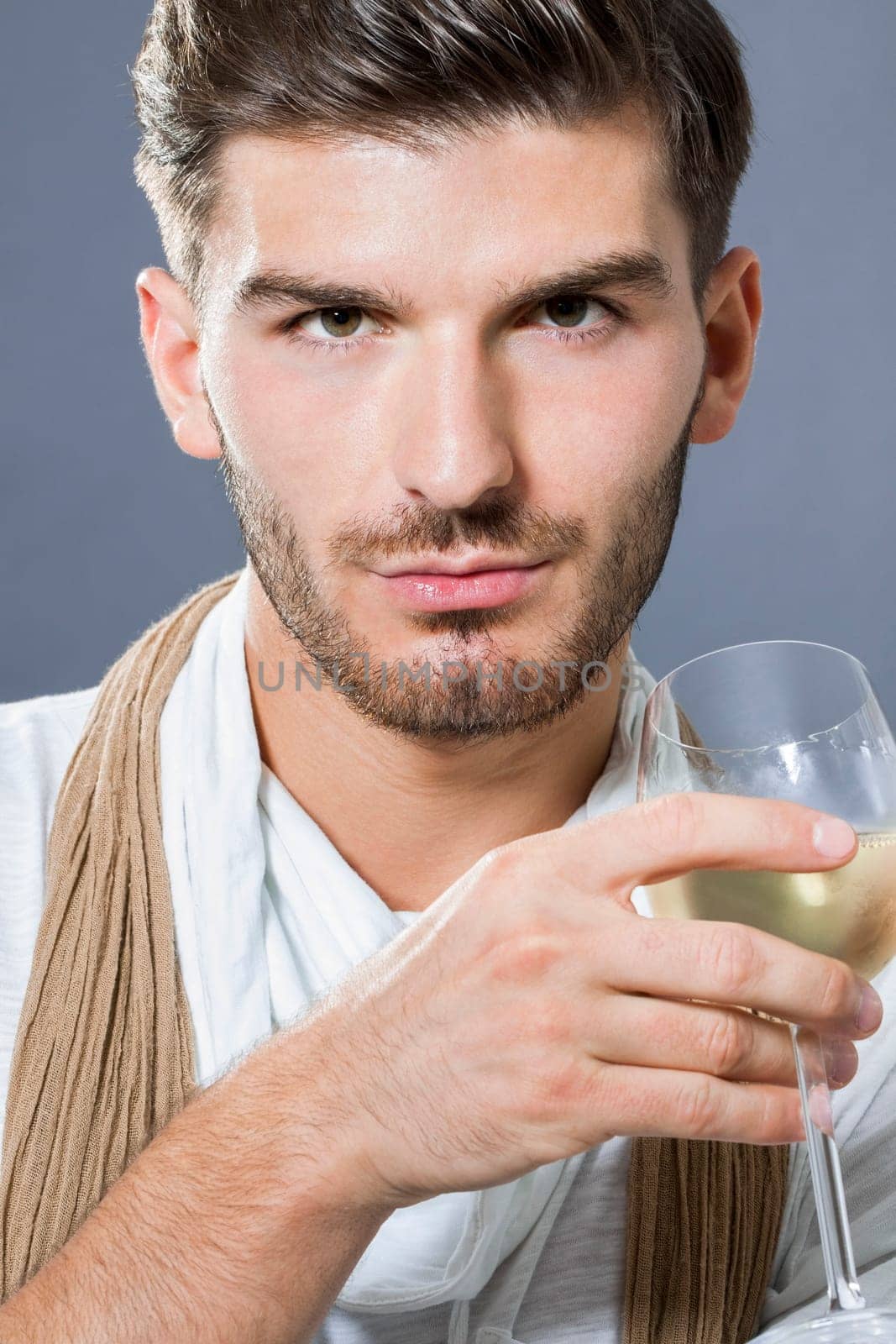 attractive young man with elegant swearing and scarf with a wine glass in his hand against a grey background