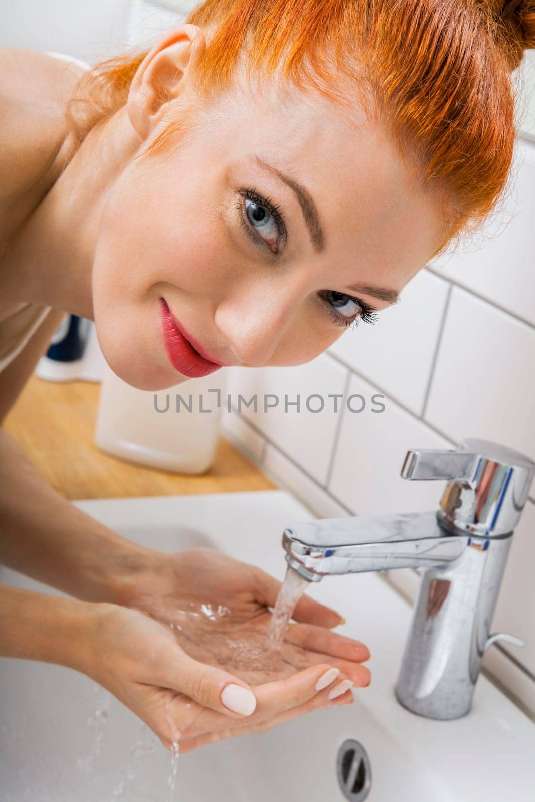 Portrait of an attractive young woman with red hair in the morning in the bathroom while washing face skin care
