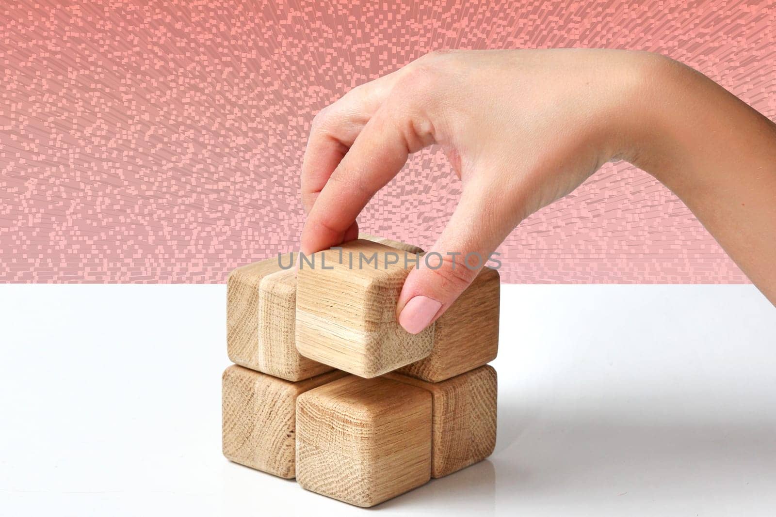On a white table, the businesswoman‘s hand arranges the last wooden block into a complete cube, Business strategy, growth process, leadership and success. Abstract cube block pattern background.